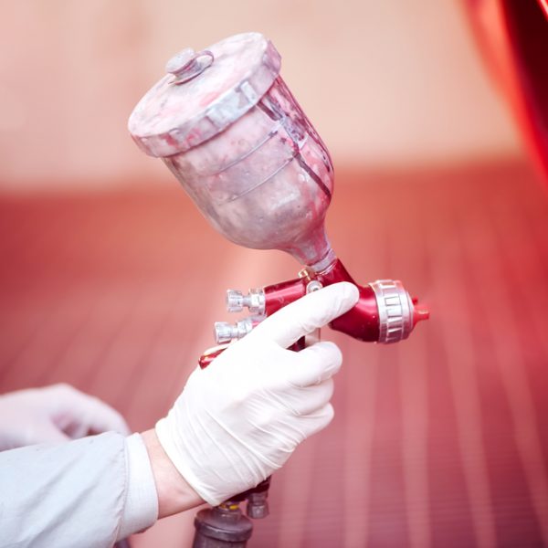 Worker painting a red car in paiting booth using professional tools and spray gun